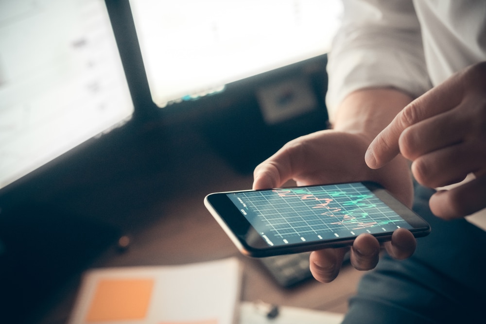 Man,Holds,Phone,In,Hand,And,Checks,Sales,Charts - Tokenhell