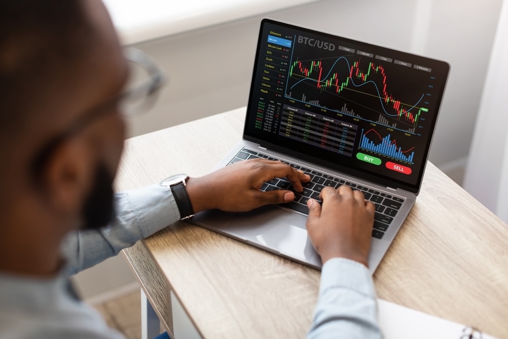 High-angleBackViewOfBlackBusinessmanUsingLaptopTypingOn - Tokenhell Revue de Bitfinancial – Un Broker en Ligne Fiable Pour Vos Investissements