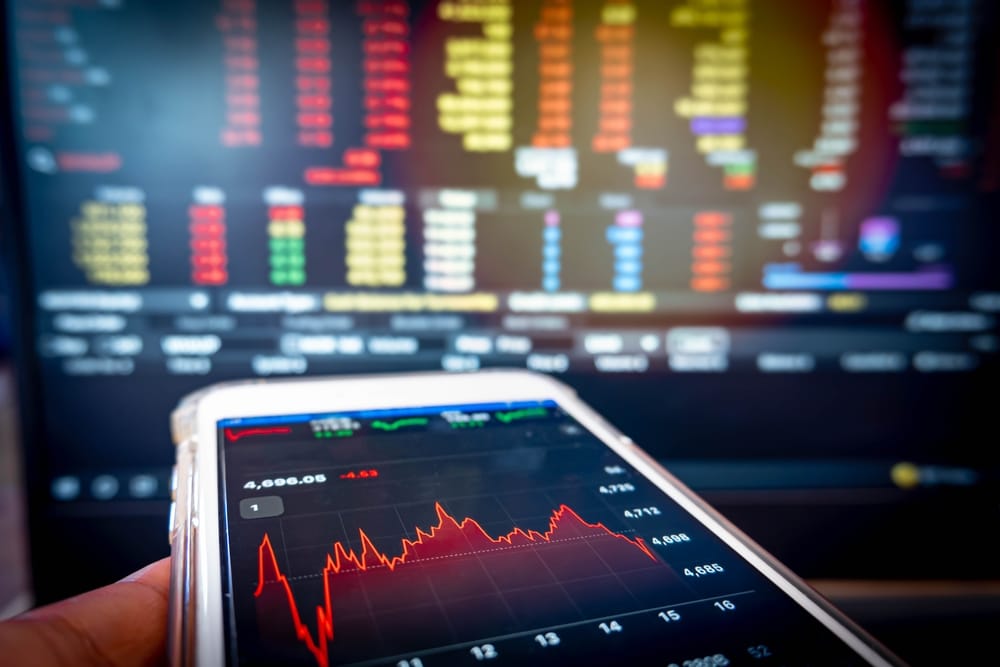 BusinessmanHoldingPhoneCheckingStockMarketDataOnComputerScreen - Tokenhell