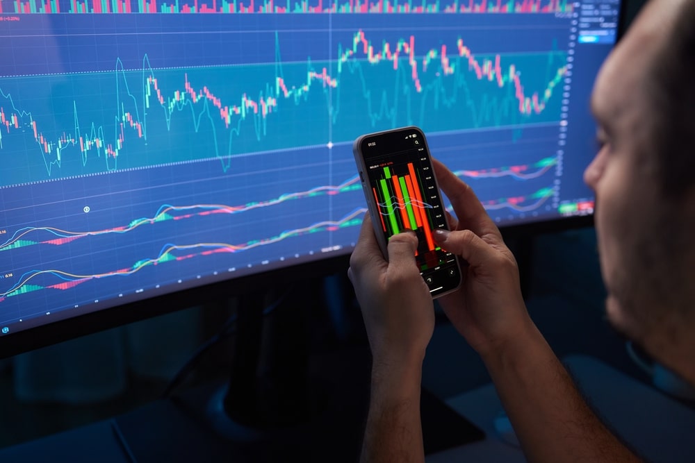 CryptoTraderInvestorBrokerHoldingFingerUsingCellPhoneApp - Tokenhell Equity Gates Review: Get To Know The Trading Broker Better